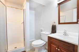 Bathroom with toilet, a stall shower, vanity, and baseboards