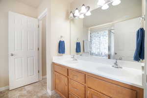 Main Bathroom with baseboards, a shower with shower door, double vanity, and a sink