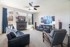 Living area with a ceiling fan, carpet flooring, baseboards, and a glass covered fireplace