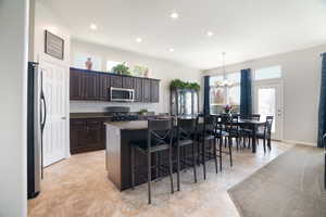 Kitchen with a breakfast bar area, appliances with stainless steel finishes, a chandelier, dark countertops, and an island with sink