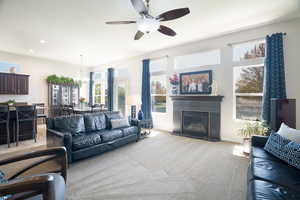 Living room with a fireplace with flush hearth, light colored carpet, baseboards, recessed lighting, and ceiling fan with notable chandelier