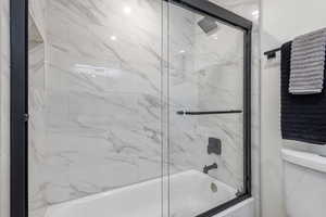 Main level hallway full bathroom featuring combined bath / shower with premium glass door and toilet