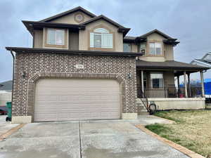 View of front of home with stucco siding, driveway, a porch, an attached garage, and brick siding