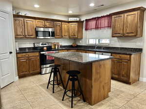 Kitchen with a center island, light tile patterned floors, appliances with stainless steel finishes, and a sink