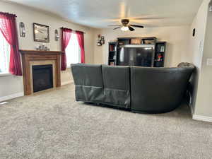 Carpeted living area with a tiled fireplace, visible vents, a ceiling fan, and baseboards