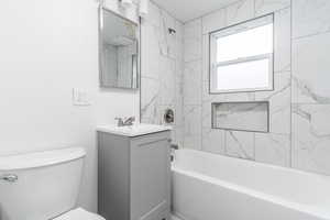 Full bath with bathtub / shower combination, toilet, vanity, and a textured wall