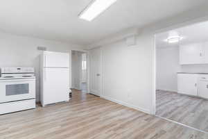 Kitchen with light wood finished floors, visible vents, baseboards, white appliances, and white cabinetry