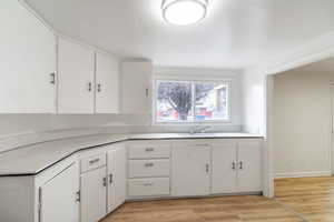 Kitchen featuring a sink, light wood-style floors, white cabinets, and light countertops