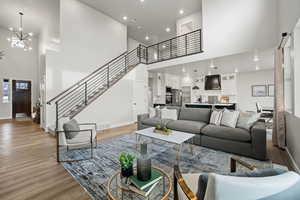 Living area with light wood-type flooring, visible vents, a notable chandelier, baseboards, and stairs