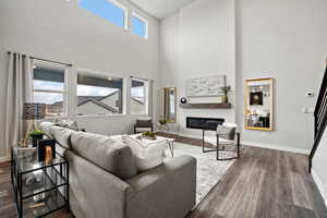 Living room featuring a glass covered fireplace, baseboards, dark wood-style flooring, and a towering ceiling