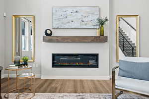 Living area featuring a glass covered fireplace, stairs, wood finished floors, and baseboards
