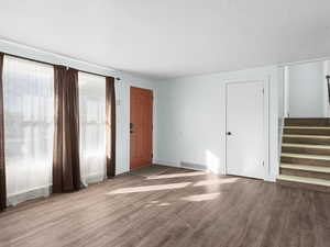 Unfurnished living room featuring stairway, wood finished floors, visible vents, and baseboards