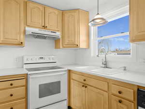 Kitchen with light brown cabinets, under cabinet range hood, light countertops, white electric range, and a sink
