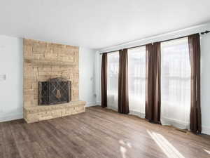 Unfurnished living room with visible vents, a stone fireplace, baseboards, and wood finished floors