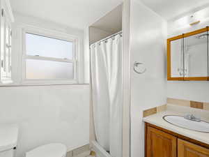 Full bath featuring a shower with shower curtain, toilet, and vanity