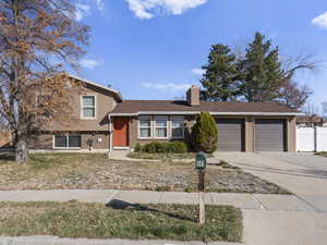 Split level home with fence, a chimney, concrete driveway, a garage, and brick siding