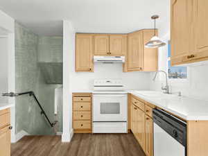 Kitchen featuring light brown cabinets, under cabinet range hood, a sink, wood finished floors, and white appliances
