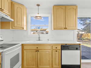 Kitchen with light brown cabinets, white appliances, under cabinet range hood, and a sink
