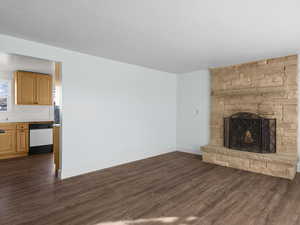 Unfurnished living room featuring dark wood finished floors, a stone fireplace, and baseboards