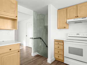 Kitchen with dark wood-type flooring, light brown cabinetry, under cabinet range hood, white electric range oven, and light countertops