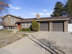 Tri-level home featuring stucco siding, a garage, concrete driveway, and a chimney