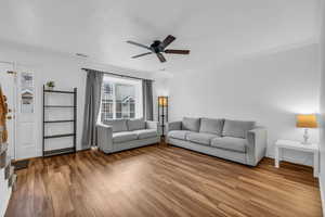 Living area with visible vents, wood finished floors, a ceiling fan, and ornamental molding
