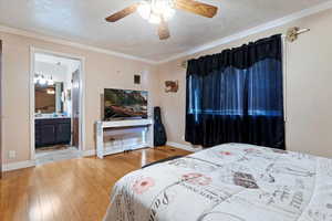 Bedroom with ensuite bath, wood finished floors, crown molding, baseboards, and ceiling fan