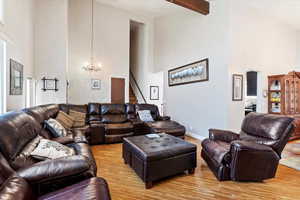 Living area with a chandelier, beamed ceiling, a towering ceiling, and light wood-style flooring