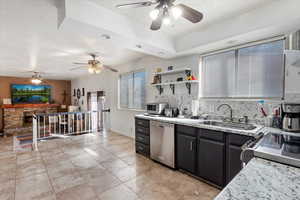 Kitchen with a sink, tasteful backsplash, stainless steel dishwasher, a stone fireplace, and light tile patterned floors