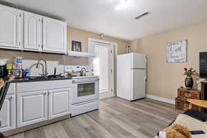 Kitchen with visible vents, dark countertops, white cabinetry, white appliances, and light wood finished floors