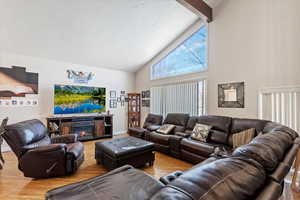 Living room featuring wood finished floors, baseboards, high vaulted ceiling, a glass covered fireplace, and beamed ceiling
