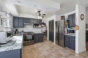 Kitchen featuring a ceiling fan, a sink, stainless steel appliances, under cabinet range hood, and backsplash