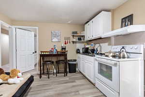 Kitchen with white electric range, under cabinet range hood, white cabinets, and a sink