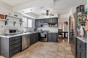 Kitchen featuring open shelves, a tray ceiling, under cabinet range hood, backsplash, and appliances with stainless steel finishes