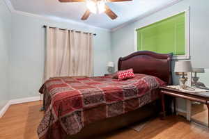 Bedroom featuring crown molding, wood finished floors, baseboards, and ceiling fan