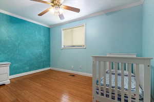Bedroom featuring visible vents, wood finished floors, baseboards, and ornamental molding