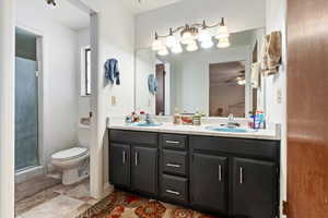 Bathroom with double vanity, toilet, ceiling fan, and a sink