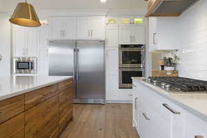 Kitchen with under cabinet range hood, built in appliances, white cabinetry, and light wood-style floors