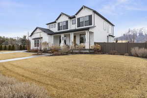 View of front of house with board and batten siding, a porch, a front yard, and fence