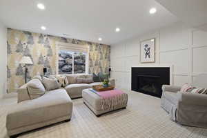 Living room featuring light carpet, a decorative wall, recessed lighting, and a glass covered fireplace