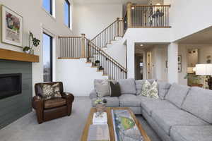 Living area featuring stairs, a glass covered fireplace, carpet flooring, and baseboards