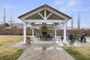 View of patio with a gazebo, an outdoor stone fireplace, and a fenced backyard