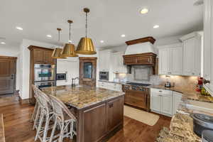 Kitchen featuring tasteful backsplash, appliances with stainless steel finishes, custom range hood, and dark wood-style flooring