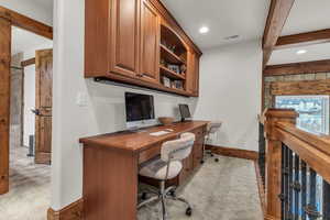 Office with beam ceiling, visible vents, a fireplace, and light carpet