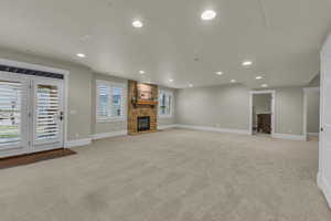 Unfurnished living room with a stone fireplace, recessed lighting, baseboards, and light carpet