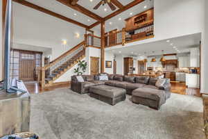 Living room with stairway, beamed ceiling, ceiling fan, and light wood finished floors