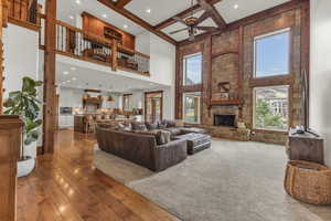 Living area featuring ceiling fan, beamed ceiling, a stone fireplace, a towering ceiling, and hardwood / wood-style flooring