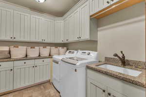 Washroom featuring cabinet space, washing machine and dryer, stone finish floor, and a sink