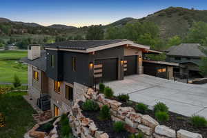 Contemporary house with stone siding, a mountain view, a chimney, driveway, and a metal roof