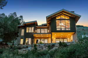 Back of house at dusk featuring a balcony and stone siding